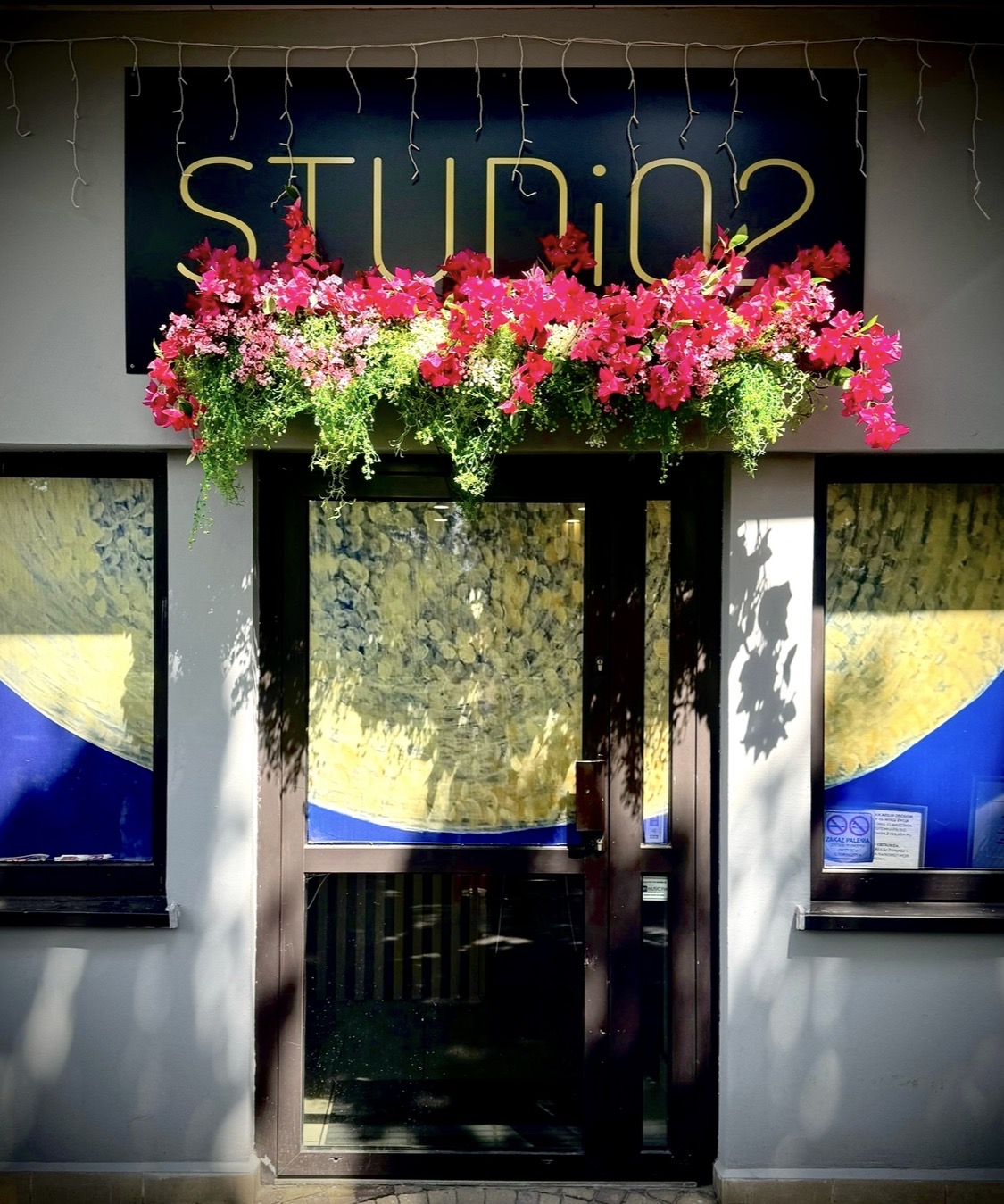 Wejście do STUDiO2 z szyldem i różowymi kwiatami